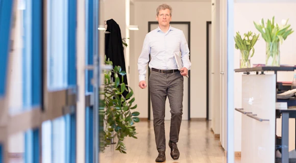 Rechtsanwalt Andreas Wollweber geht einen Flur entlang, ein Notebook unter dem Arm.